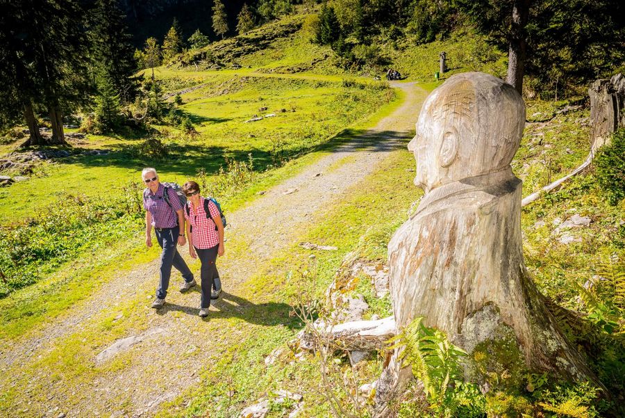 Wanderer vor einer Holzskulptur auf dem Schnitzlerweg auf der Axalp im Sommer