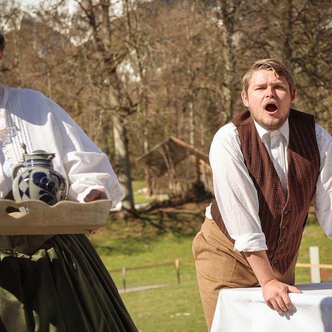 Ein Mann an einem Tisch schreit einer Frau hinterher welche mit Getränken davonläuft.