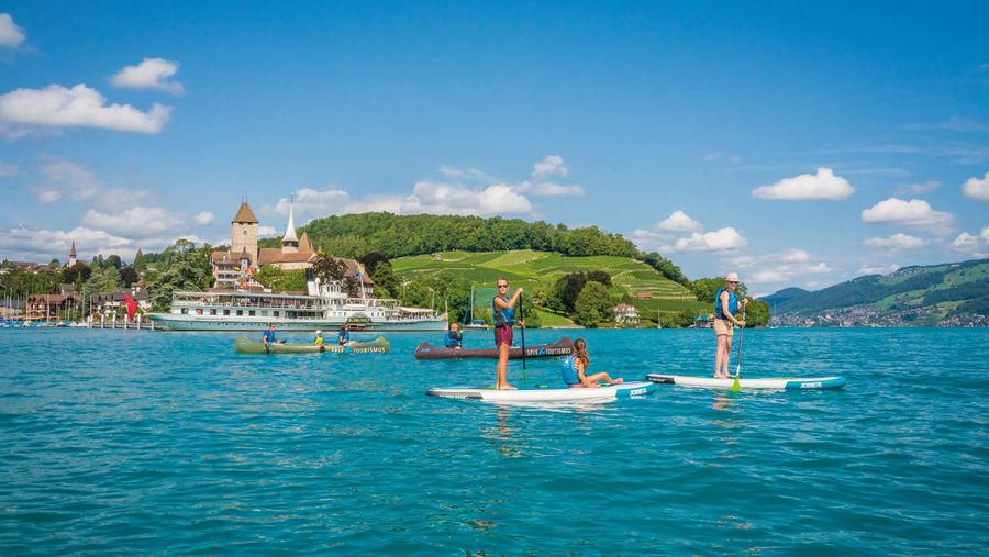 Freunde gleiten über das tiefblaue Wasser und geniessen die umliegende grüne Naturlandschaft und den Ausblick auf das Schloss Spiez