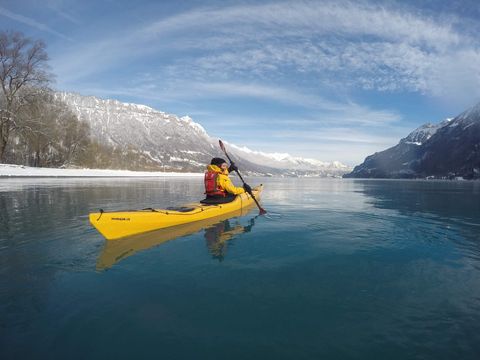Frau in einem gelben Kajak auf dem Brienzersee umgeben von verschneiten Berge