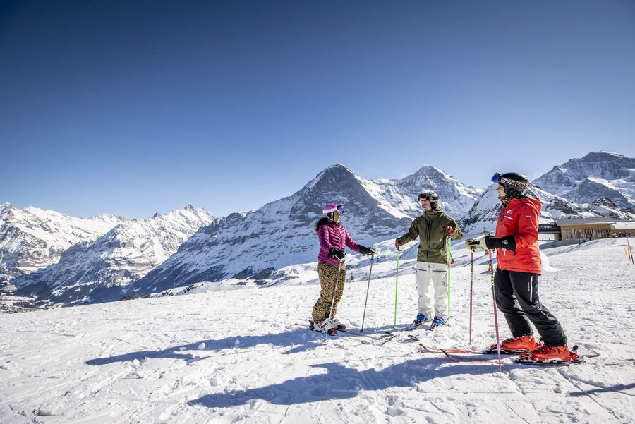 Eine Gruppe Skifahrer geniesst das Bergpanorama von Eiger, Mönch und Jungfrau und steht auf den Skiern, fertig für die nächste Abfahrt, im Schnee. 