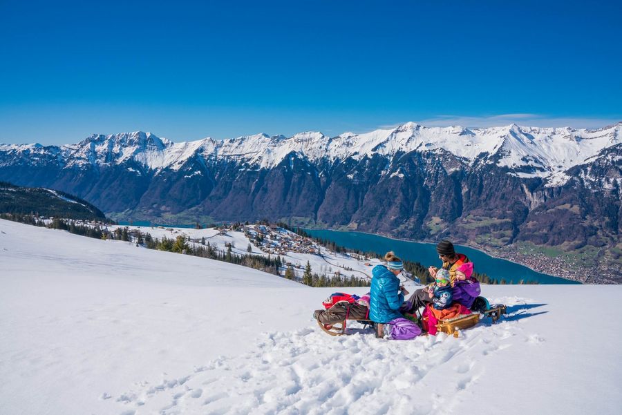 Familie macht Pause während dem Schlittenfahren auf der Axalp mit Blick auf den Brienzersee und die Berge