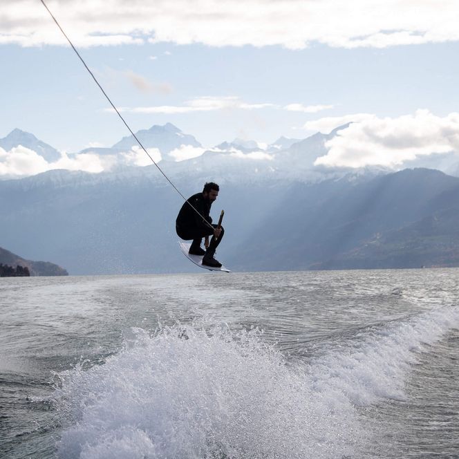 Ein Wakeboarder vollzieht einen Sprung vor der Bergkulisse des Thunersees. 