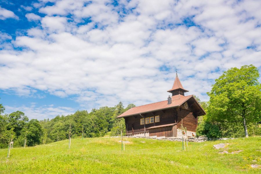 Mitten auf einer saftig grünen Wiese steht ein traditioneller Spycher. Schäfchenwolken zieren den blauen Himmel.