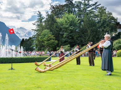 Alphornbläser im Kursaal Garten Interlaken Alphornspieler auf grüner Wiese vor Wasserspiel im Kursaal Garten Interlaken