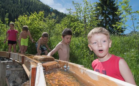 Kinder beobachten auf dem Wasserspielplatz die Dynamik des Wassers in einem Holzkännelsystem