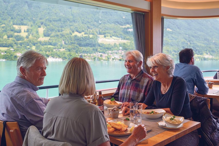 4 lachende Freunde sitzen beim Hauptgang im Schiffsrestaurant auf der Genusstour Brienzersee