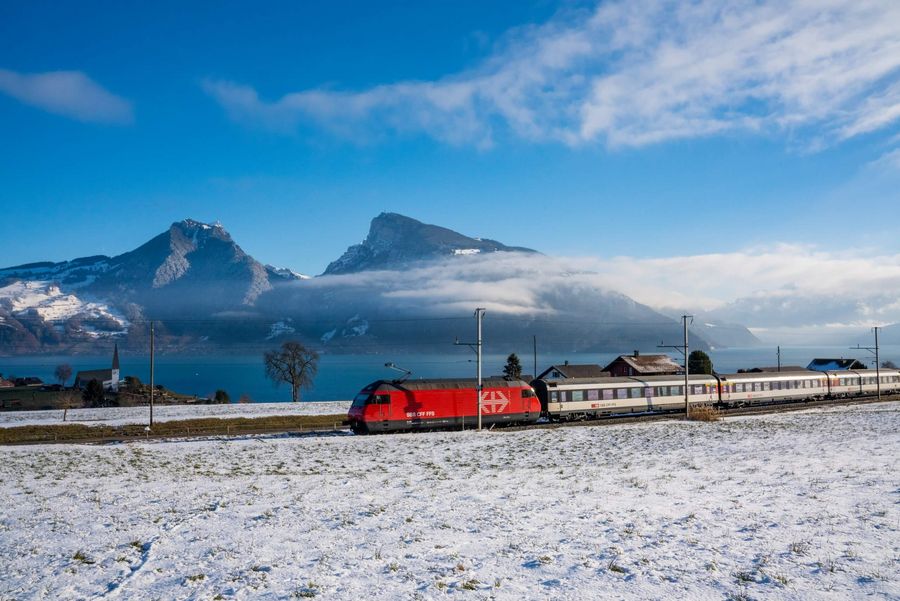 BLS Zug fährt durch die Winterlandschaft entlang des Thunersees von Interlaken nach Spiez. Im Hintergrund das verschneite Niederhorn.
