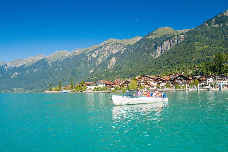 Familie gleitet im Motorboot über den türkisfarbenen Brienzersee. Im Hintergrund ist das Schnitzlerdorf Brienz zu sehen.