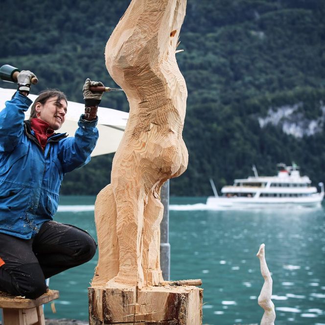 Holzbildhauerin schnitzt an ihrem Kunstwerk aus Holz vor dem türkisen Brienzersee