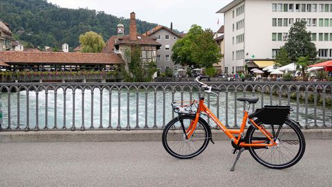 Frau fährt mit rotem Leihvelo entlang der Aare durch die Stadt Thun
