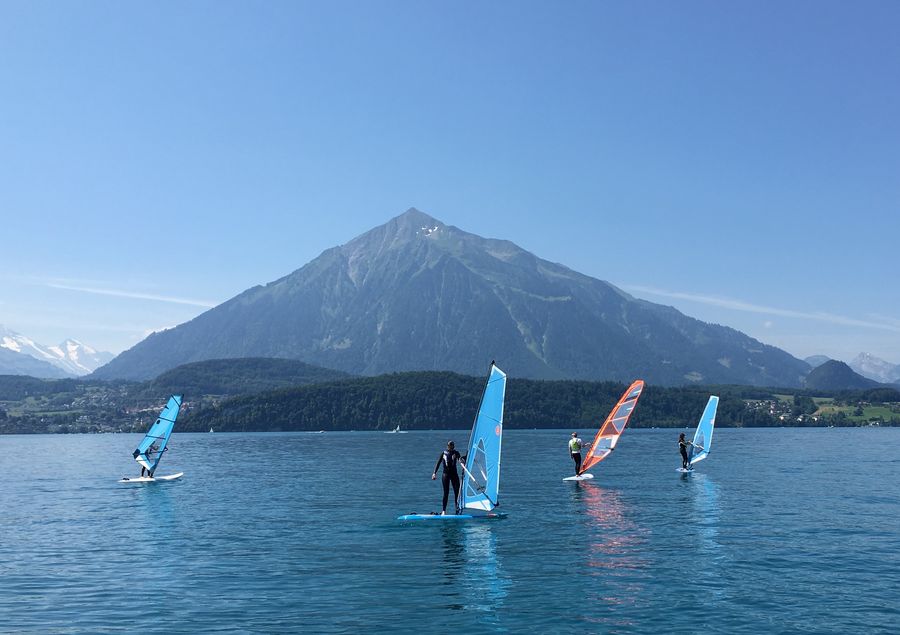 Eine Gruppe von Windsurfern auf dem blauen Thunersee vor dem pyramidenförmigen Niesen