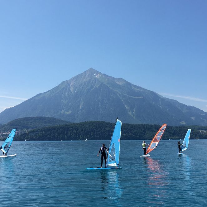Eine Gruppe von Windsurfern auf dem blauen Thunersee vor dem pyramidenförmigen Niesen
