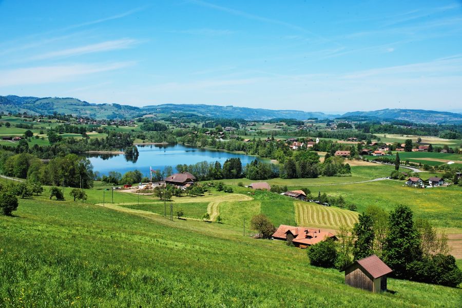 Tiefblauer Amsoldingersee inmitten prächtiger Naturlandschaft und mit Kirche, Dorf und kleinen Alphütten.