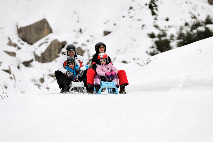 Familie fährt mit dem Schlittel durch die tiefverschneite Winterlandschaft auf dem Schlittelweg in Saxeten