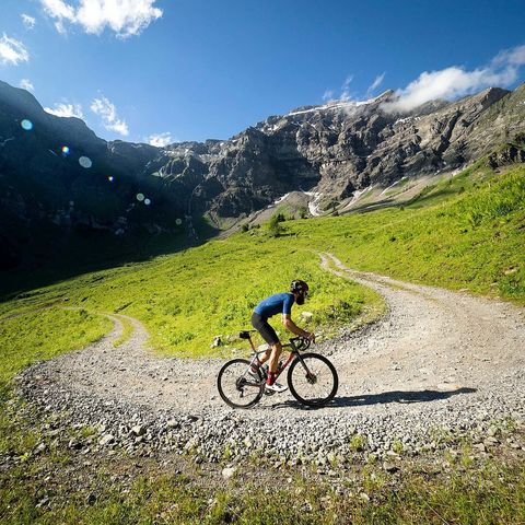 Biker unterwegs auf einer Naturstrasse mit grünen Alpwiesen und Felsen im Hitergrund