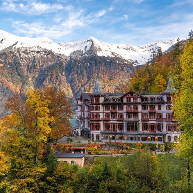 Das altehrwürdige Grandhotel Giessbach umgeben vom herbstlichen Wald, im Hintergrund verschneite Berggipfel.