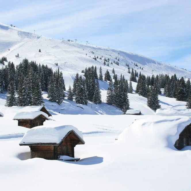 Verschneite Axalp mit Alphütten und Tannen sowie Skilift im Hintergrund