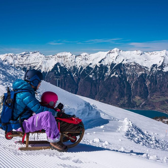 Familie am Schlittenfahren auf der Axalp mit Aussicht auf die verschneiten Berge