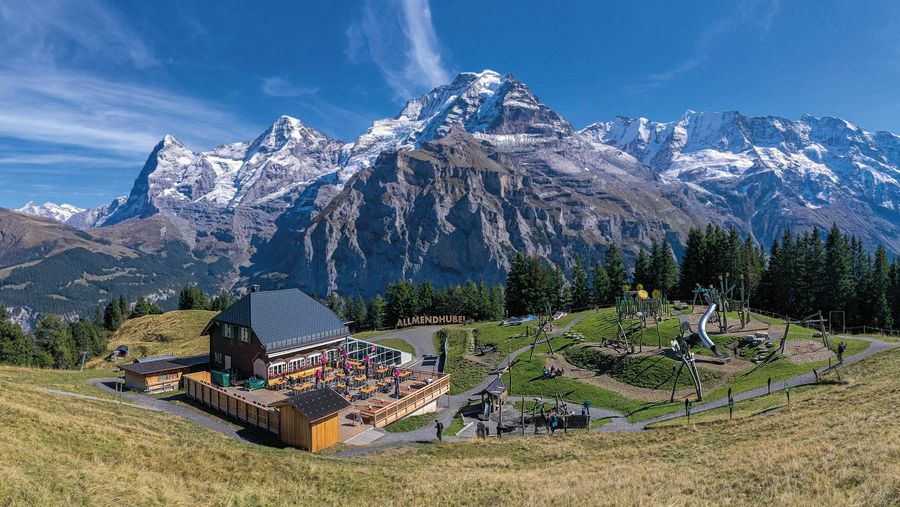 Frühlingswiese mit Bergrestaurant Allmendhubel und Bergen im Hintergrund