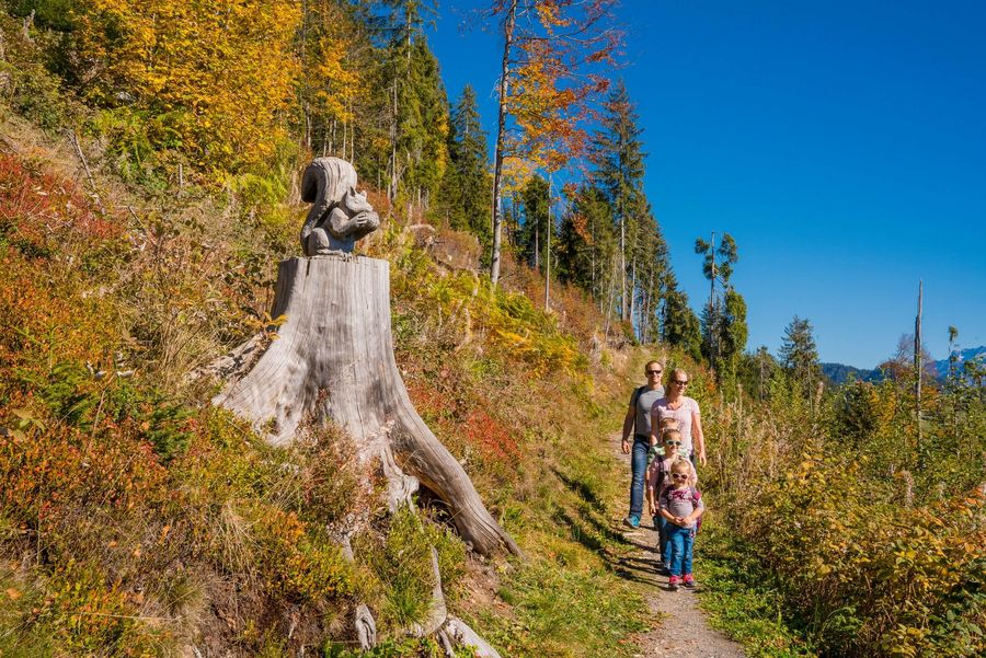 Familie auf einem Wanderweg mit einer Holzskulptur im Herbst in Beatenberg