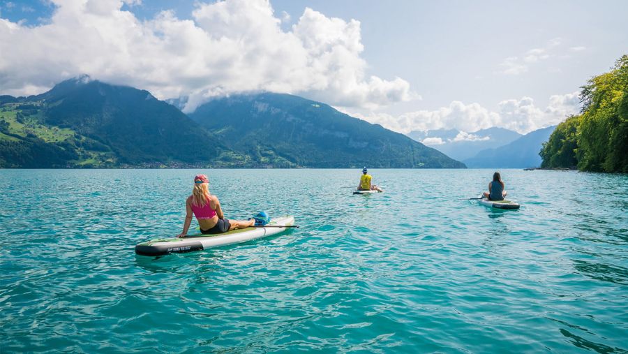 Drei Freunde relaxen auf dem Thunersee auf Stand Up Paddle Boards und geniessen den Blick auf die Bergwelt