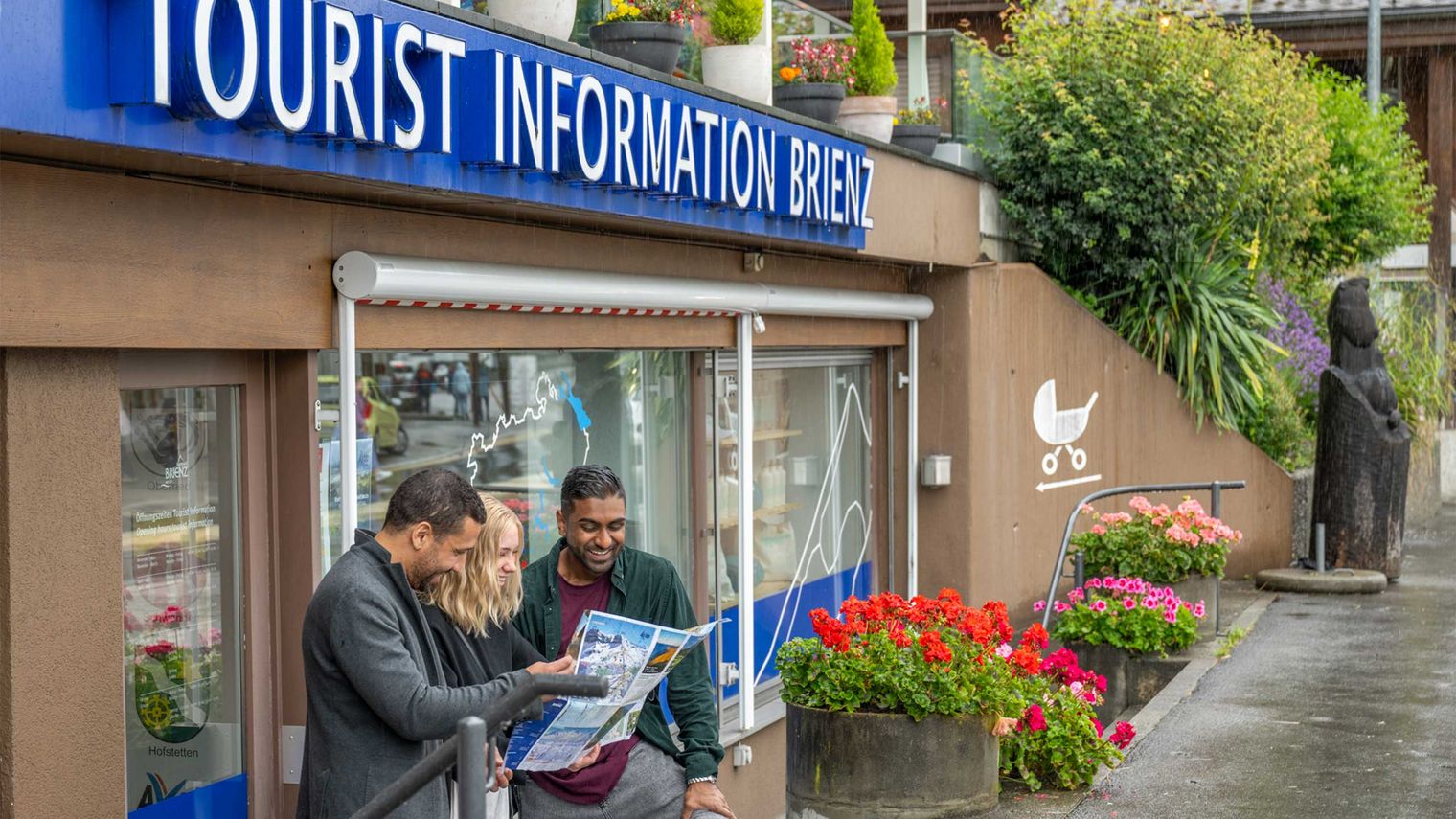 Gäste sturdieren einen Prospekt vor der Tourist Information von Brienz Tourismus