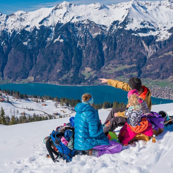 Familie macht Pause im Schnee während dem Schlittelplausch mit Blick auf den Brienzersee